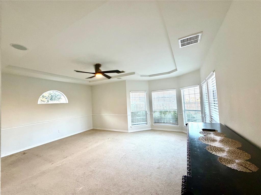Tray ceiling with integrated recessed lighting, expansive bay windows, arched accent window, and ceiling fan