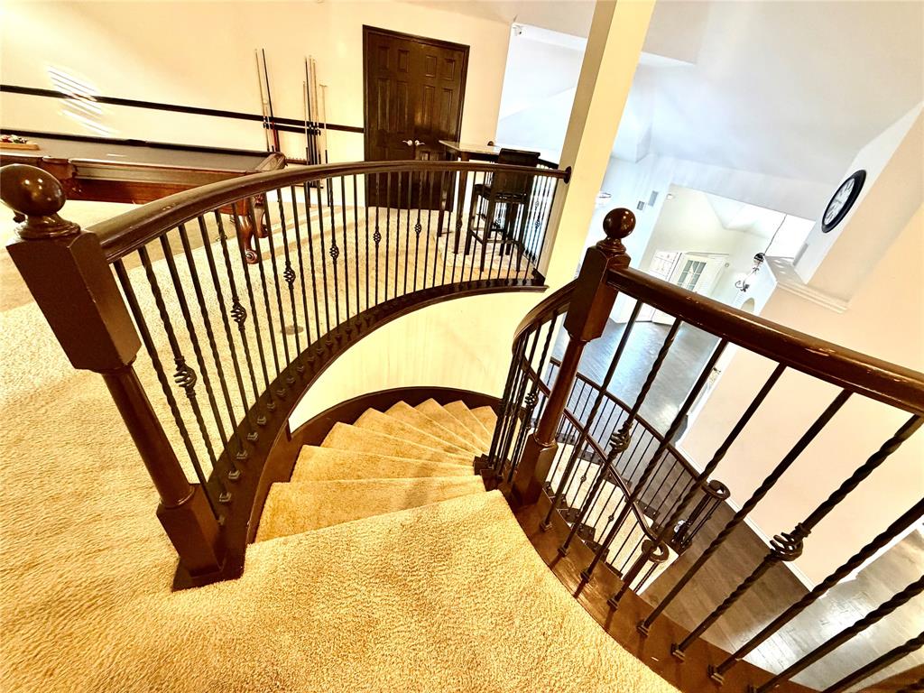 Curved staircase featuring custom wrought iron balusters, a dark wood-finish handrail, carpeted treads, and architectural vaulted ceilings