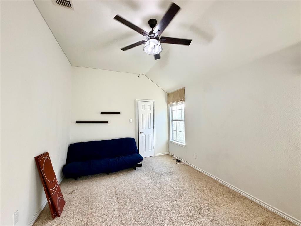 Vaulted ceiling featuring a central five-blade ceiling fan with integrated lighting, wall-mounted floating shelving, and a single-pane window with grid detailing