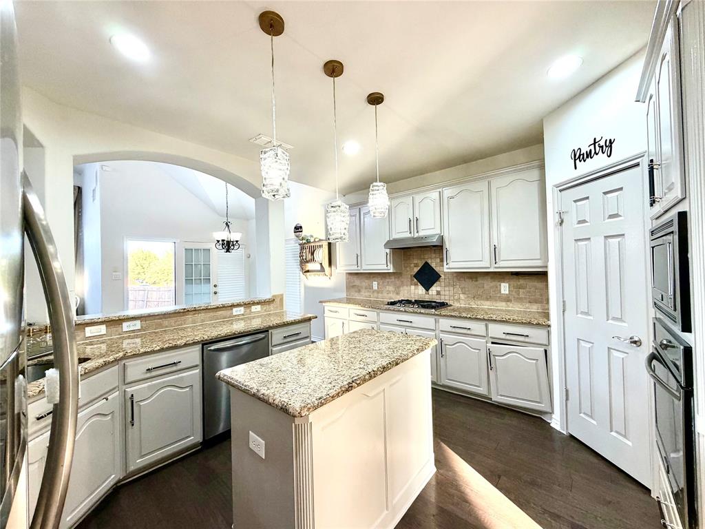 Kitchen featuring light-toned cabinetry, stone-finish countertops, tile backsplash, wood-finish flooring, and a center island with three glass pendant lights