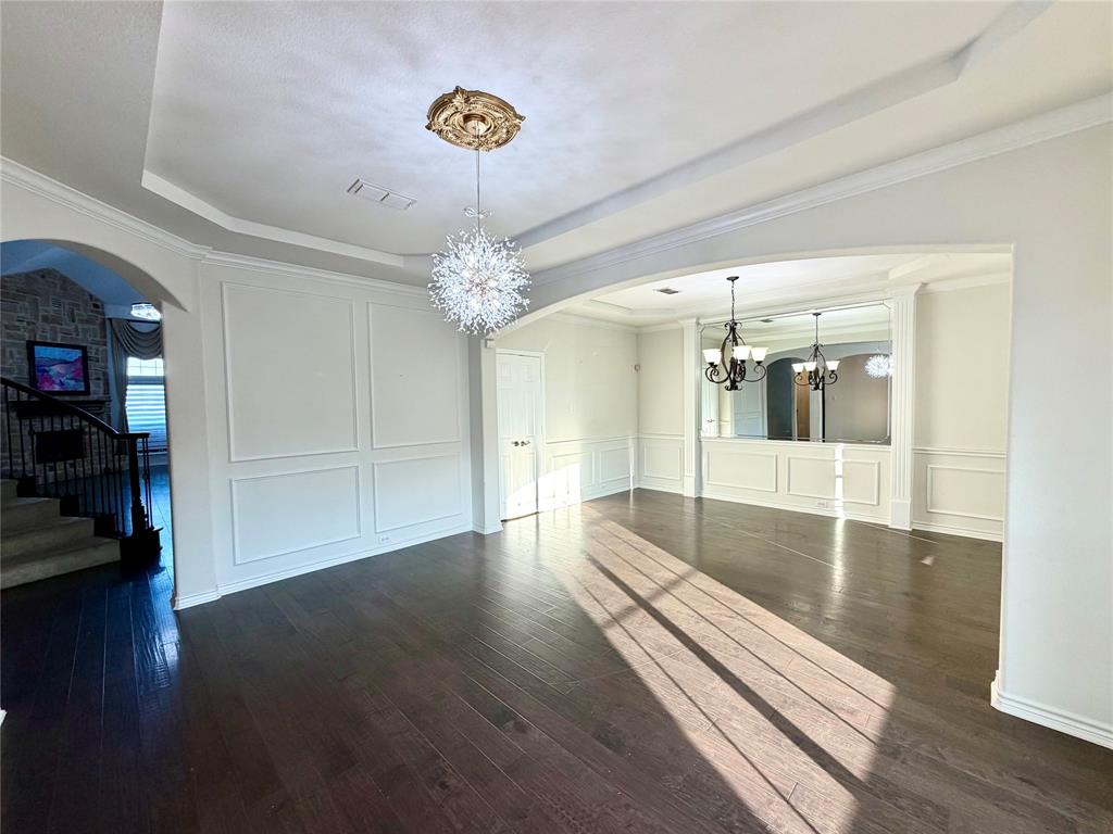 Tray ceiling with central medallion, wood-finish flooring, wainscoting paneling, multi-tiered crystal-style chandelier, and recessed lighting