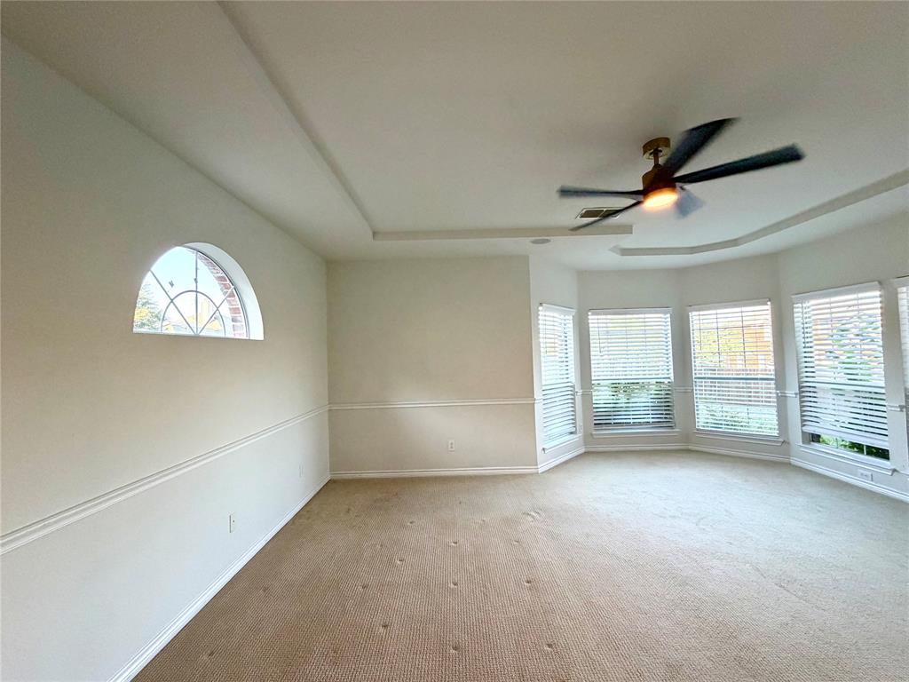 Tray ceiling with a central multi-blade light fixture, arched accent window, chair rail molding, and multiple windows with horizontal blinds