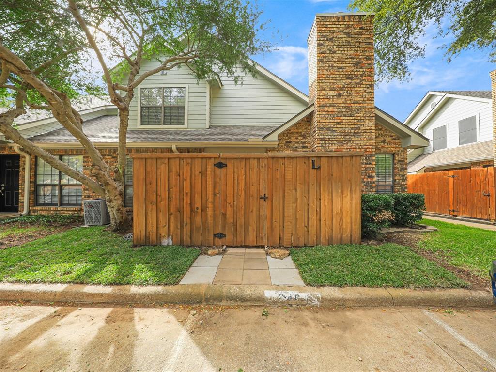 Exterior elevation featuring a brick and horizontal siding facade, a prominent brick chimney, and a wooden privacy fence with a stone-paved walkway Exterior elevation featuring a brick and horizontal siding facade, a prominent brick chimney, and a wooden privacy fence with a stone-paved walkway