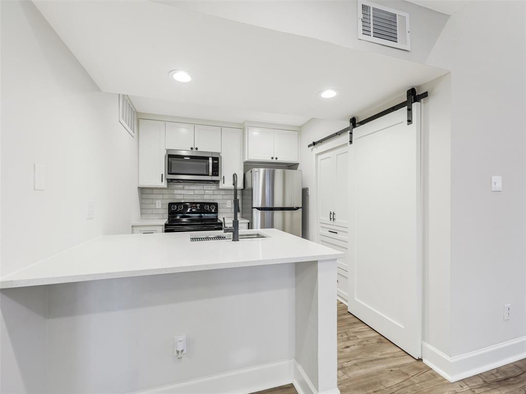 Kitchen featuring a stone-surface breakfast bar, white cabinetry, stainless steel appliances, subway tile backsplash, and a sliding barn door