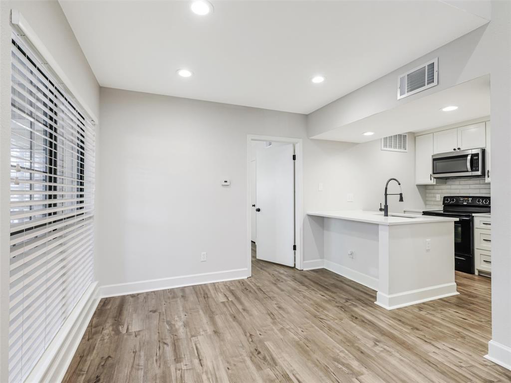 Wood-finish flooring, recessed lighting, white cabinetry, matte black hardware, and a breakfast bar Wood-finish flooring, recessed lighting, white cabinetry, matte black hardware, and a breakfast bar