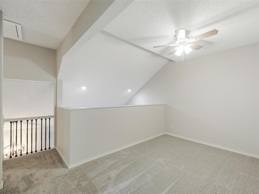 Vaulted ceiling, neutral wall tones, textured ceiling finish, ceiling fan with light fixture, and black metal spindle railing