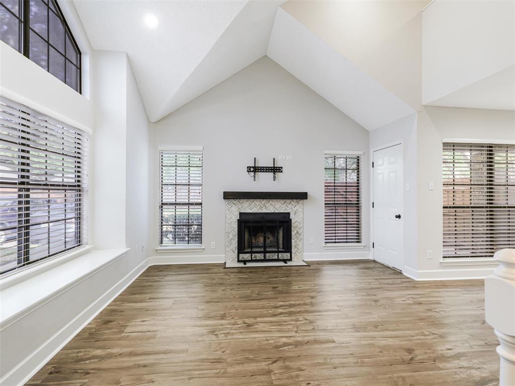 Vaulted ceilings featuring a fireplace with a chevron-pattern tile surround and a dark wood mantel, wood-finish flooring, and expansive windows with built-in window seating Vaulted ceilings featuring a fireplace with a chevron-pattern tile surround and a dark wood mantel, wood-finish flooring, and expansive windows with built-in window seating
