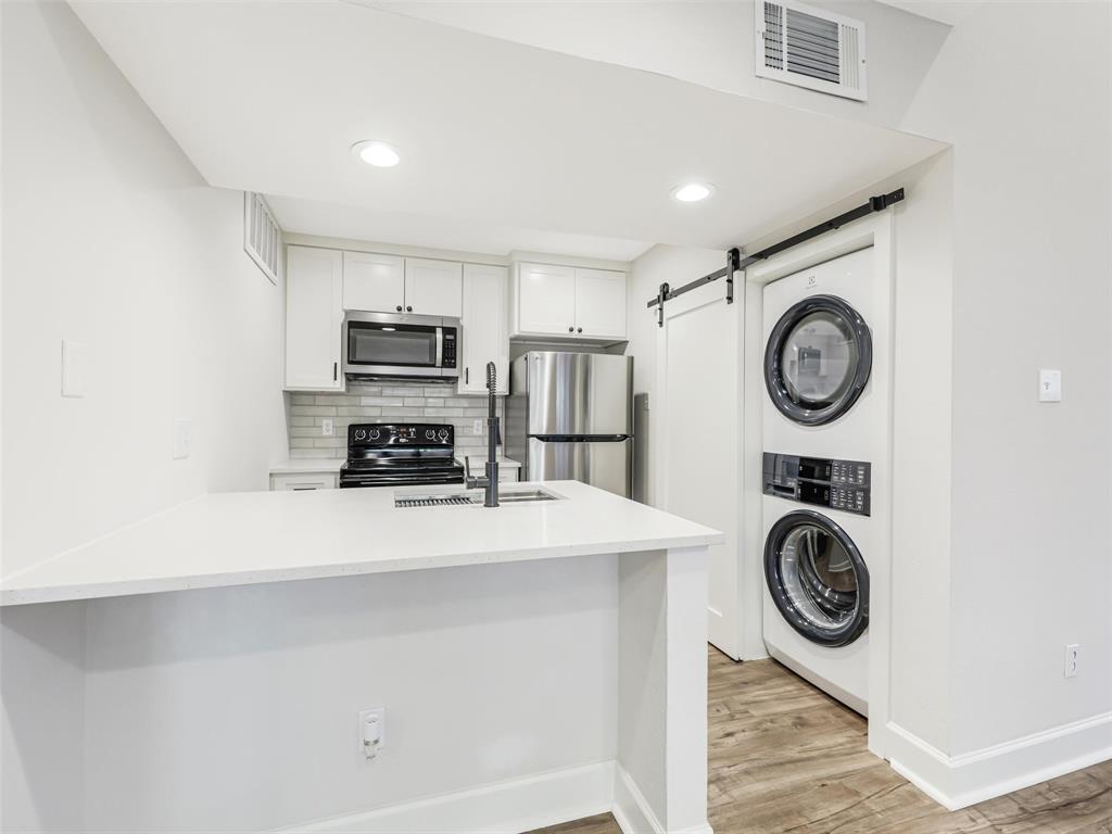 Kitchen featuring white cabinetry, solid-surface countertops, subway tile backsplash, stainless steel appliances, and wood-finish flooring with a barn-style sliding door concealing a laundry area