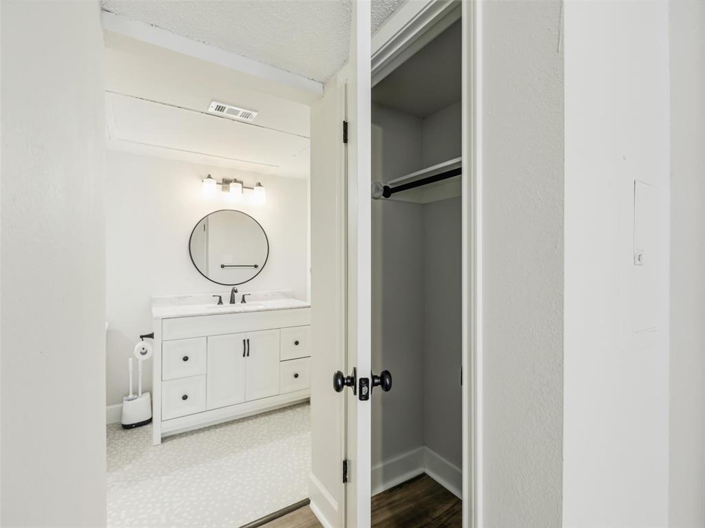 Bathroom featuring a white vanity with drawers, a round mirror, three-light fixture, and patterned flooring, complemented by a storage closet with a built-in rod and shelf