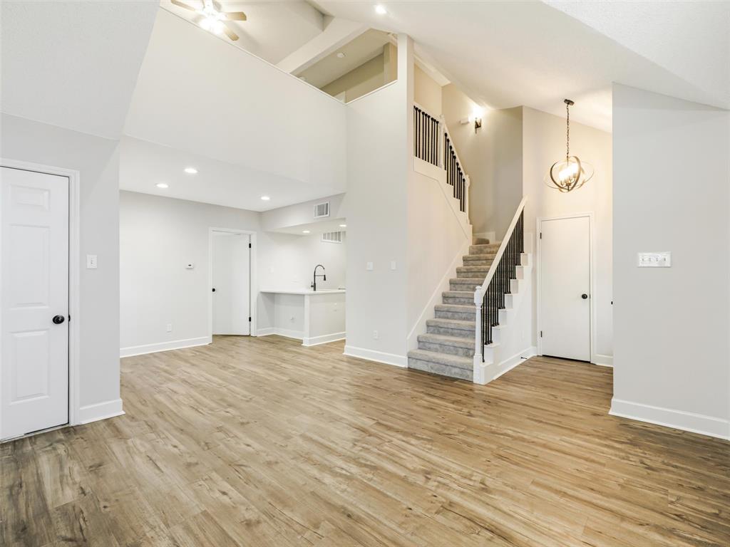 Vaulted ceilings with recessed lighting, wood-finish flooring, staircase with a matte black railing, orb-style pendant lighting, and an integrated wet bar Vaulted ceilings with recessed lighting, wood-finish flooring, staircase with a matte black railing, orb-style pendant lighting, and an integrated wet bar