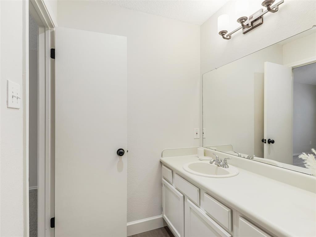 Vanity with a solid-surface countertop and integrated basin, large wall-mounted mirror, and multi-bulb vanity light fixture
