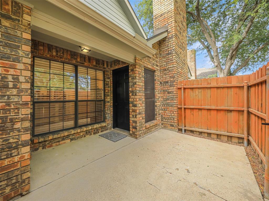 Brick exterior patio featuring a concrete slab, floor-to-ceiling brick chimney, dark-trimmed windows, and a wood privacy fence