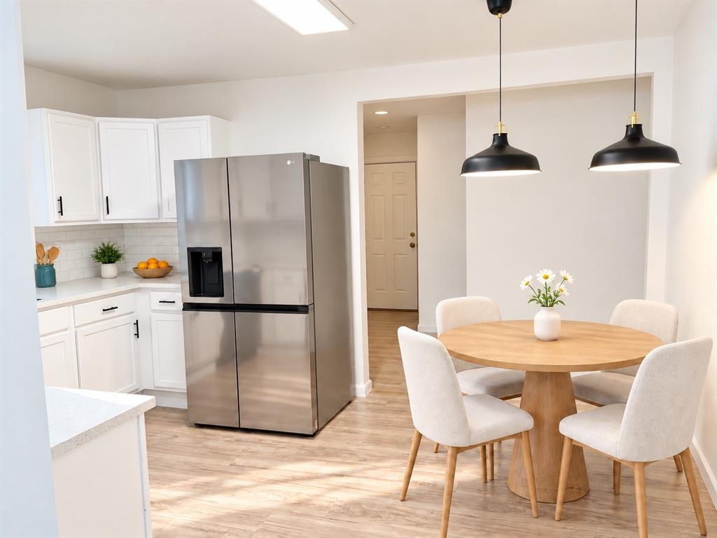 Kitchen featuring white shaker-style cabinetry, light-toned countertops, subway tile backsplash, stainless steel multi-door refrigerator, and matte black pendant lighting over the dining area with wood-finish flooring