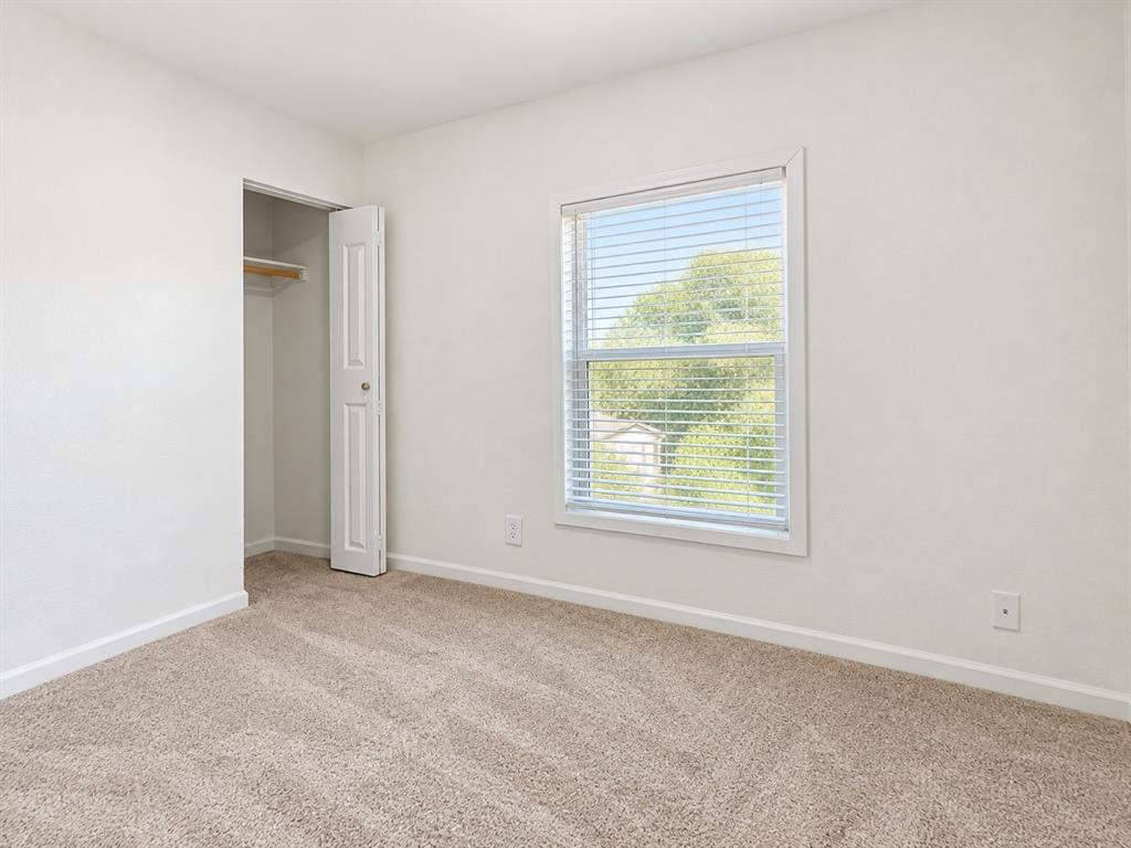 Neutral-toned carpeting, crisp wall finishes, single-hung window with fitted blinds, and a built-in closet featuring a hinged door