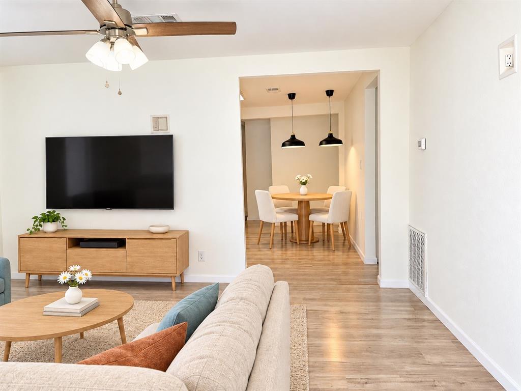 Neutral interior featuring wood-finish flooring, a ceiling fan with integrated lighting, and dual matte black pendant fixtures