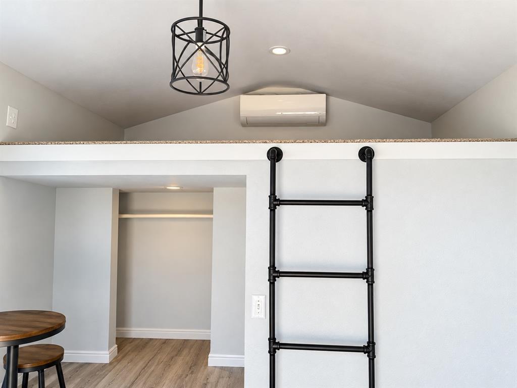 Loft area featuring a neutral stone-look ledge, black industrial-style pipe ladder, wall-mounted climate control unit, and a black open-cage pendant fixture