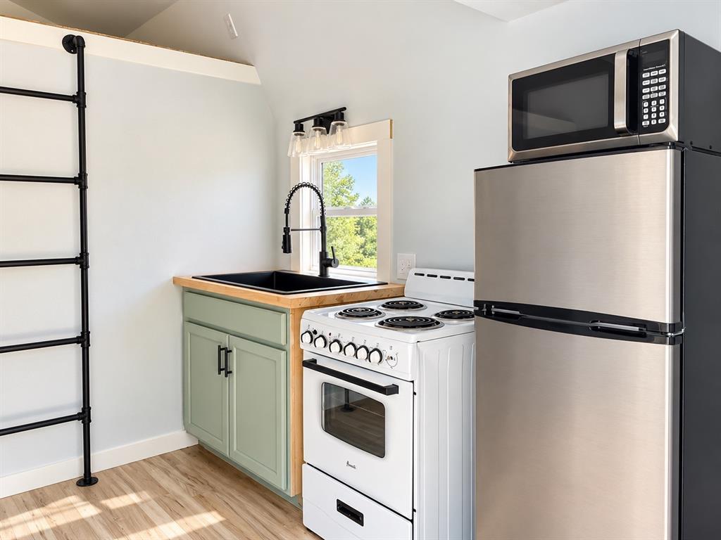 Compact kitchen featuring stainless steel appliances, a black drop-in sink with a high-arc faucet, wood-finish countertops, custom cabinetry, and a floor-to-ceiling metal ladder fixture