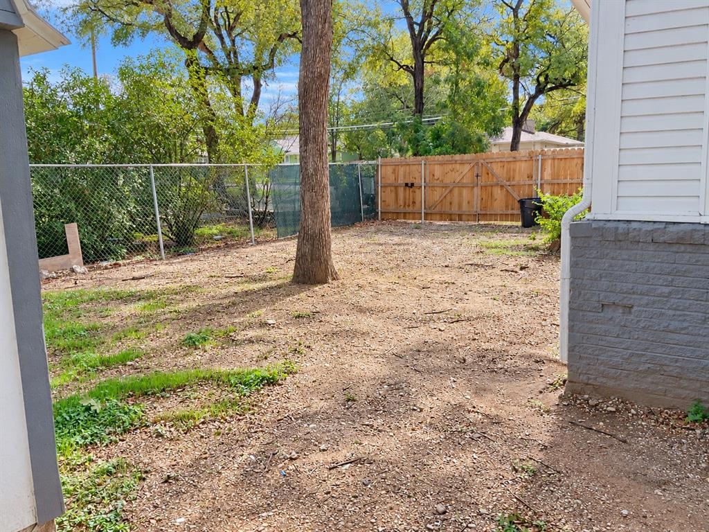 Backyard featuring a wood privacy fence, chain-link perimeter fencing, and mature trees