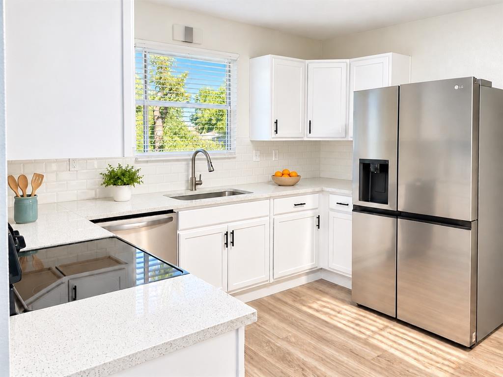 Kitchen featuring white shaker-style cabinetry, light-toned stone-finish countertops, stainless steel appliances, subway tile backsplash, and wood-finish flooring
