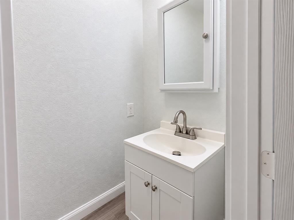 White vanity featuring a solid surface countertop with an integrated basin, satin nickel faucet, shaker-style cabinetry, and a matching mirrored medicine cabinet, complemented by wood-finish flooring