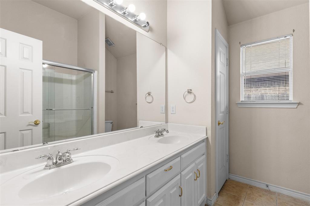 Double vanity featuring white cabinetry, integrated sinks with polished chrome fixtures, expansive wall-mounted mirror, and tile flooring