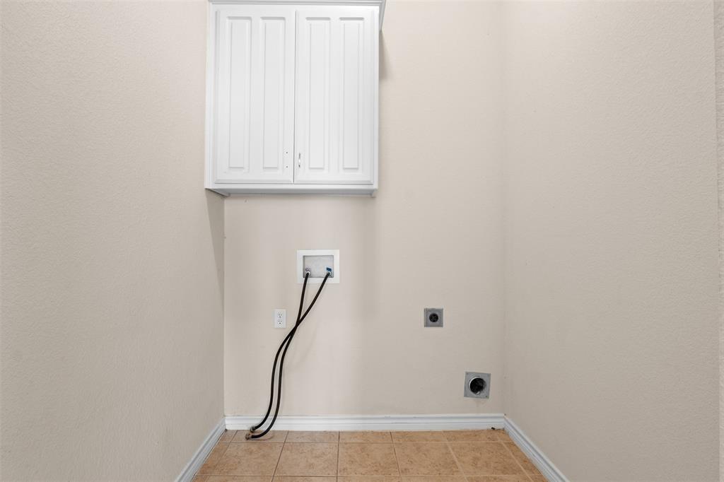 Wall-mounted white shaker-style cabinetry, ceramic tile flooring, and dedicated laundry utility hookups