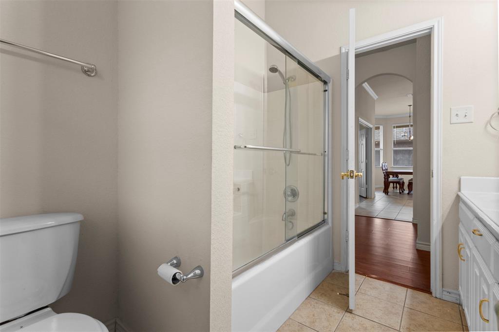 Bathroom featuring a bathtub with a sliding glass enclosure, a white vanity with hardware, tiled flooring, and a towel bar