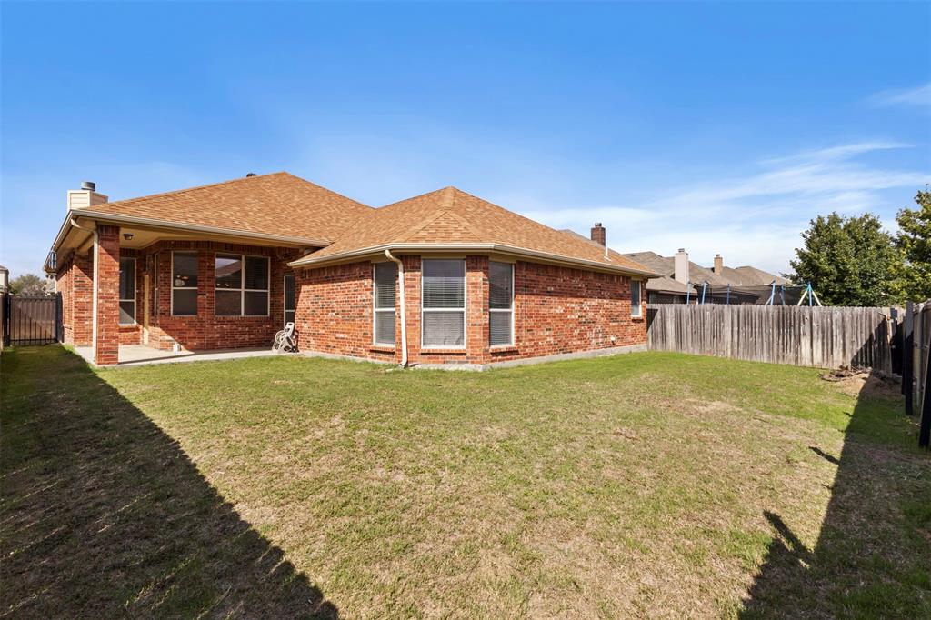 Rear exterior featuring a brick facade, shingle roof, covered patio, and wood privacy fencing