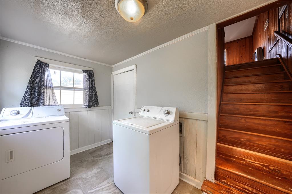 Utility room featuring tile flooring, wainscoting, and a multi-pane window, incorporating a wooden staircase with a banister