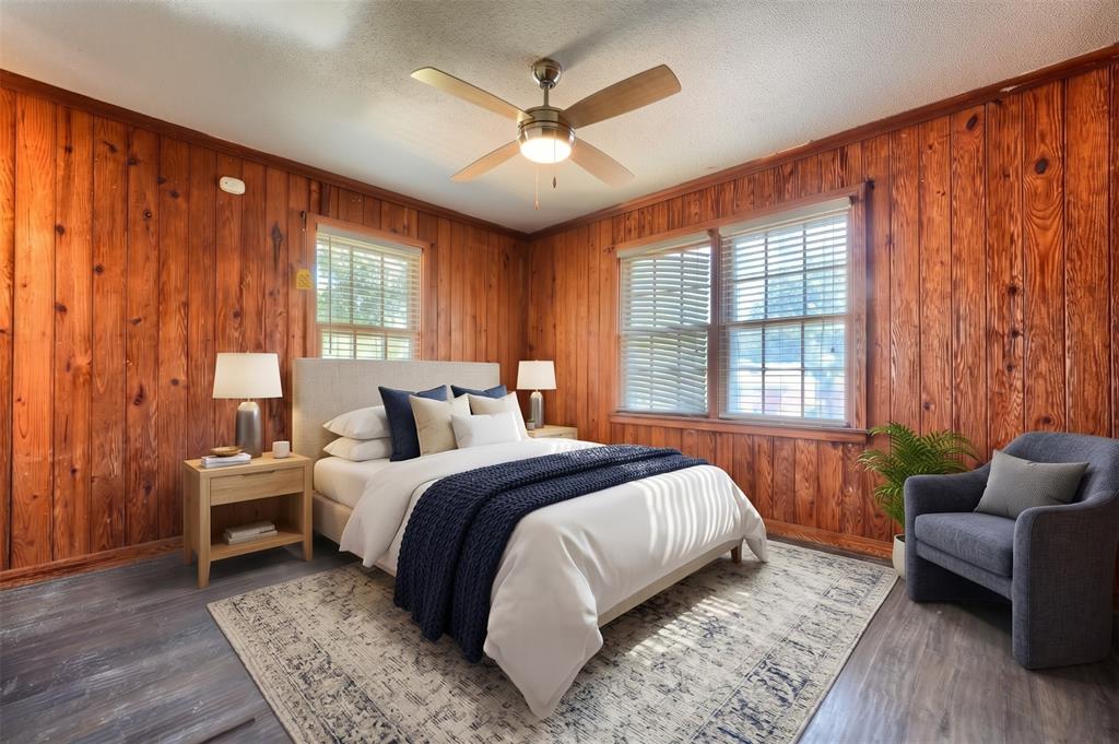 Wood-paneled walls, neutral wood-finish flooring, multi-pane windows, and a central ceiling fan with an integrated light fixture