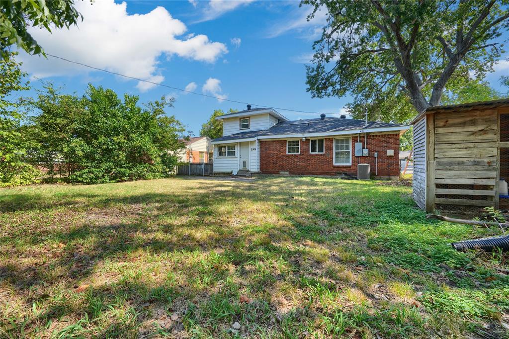Expansive backyard featuring mature trees, partial brick exterior, white siding, and a wooden storage structure