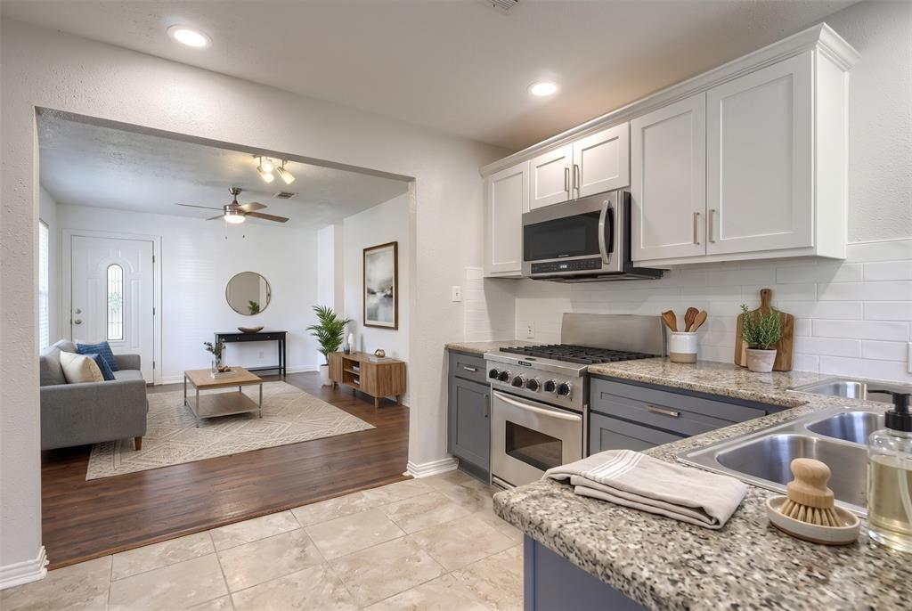 Kitchen featuring two-tone shaker-style cabinetry, speckled stone countertops, a white subway tile backsplash, and stainless steel gas range with built-in microwave