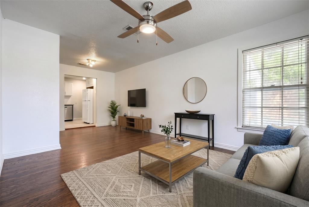 Living area featuring wood-finish flooring, a ceiling fan, and large windows with horizontal blinds