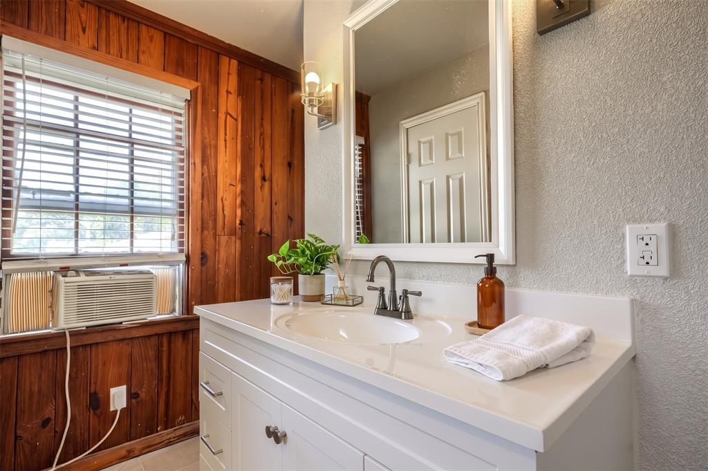 White vanity featuring an integrated basin, faucet with dual handles, wood-paneled accent wall, and wall-mounted mirror