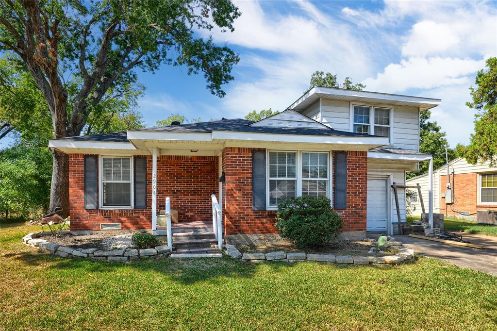 Red brick exterior featuring horizontal siding accents, stone-lined garden borders, a covered front entryway, and multi-paned windows with decorative shutters