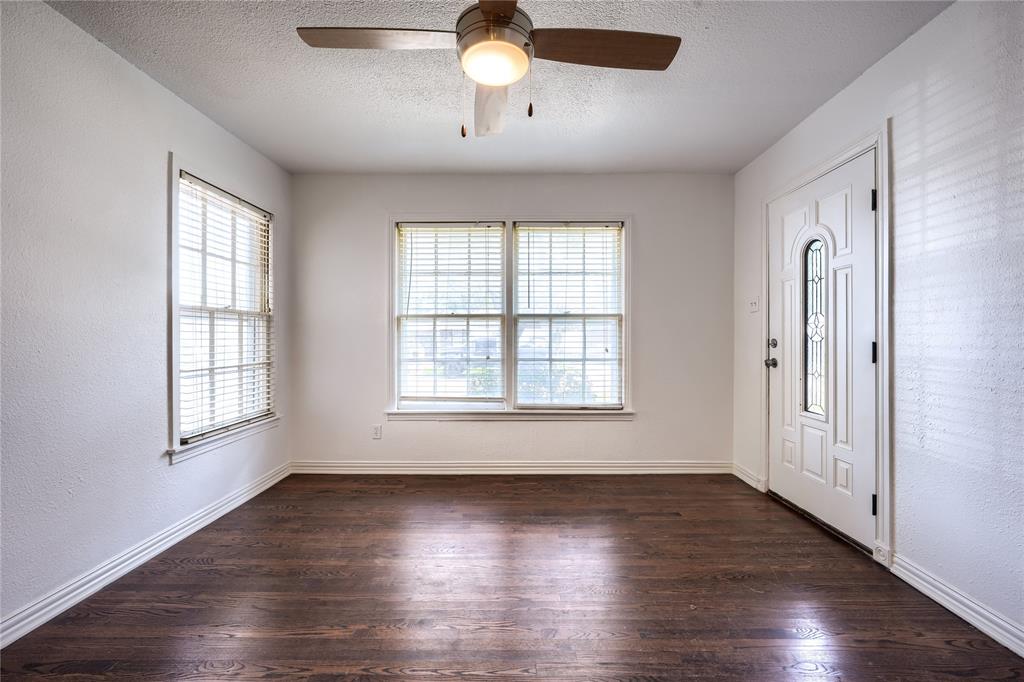 Interior space featuring dark-toned wood-finish flooring, multi-pane windows, and a white entry door with an arched glass insert, complemented by a central ceiling fan with an integrated light fixture