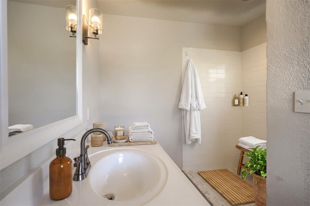 Bathroom featuring a white vanity with an oval undermount sink, oil-rubbed bronze faucet, wall-mounted light fixtures, and a walk-in shower with horizontal subway-style tiling