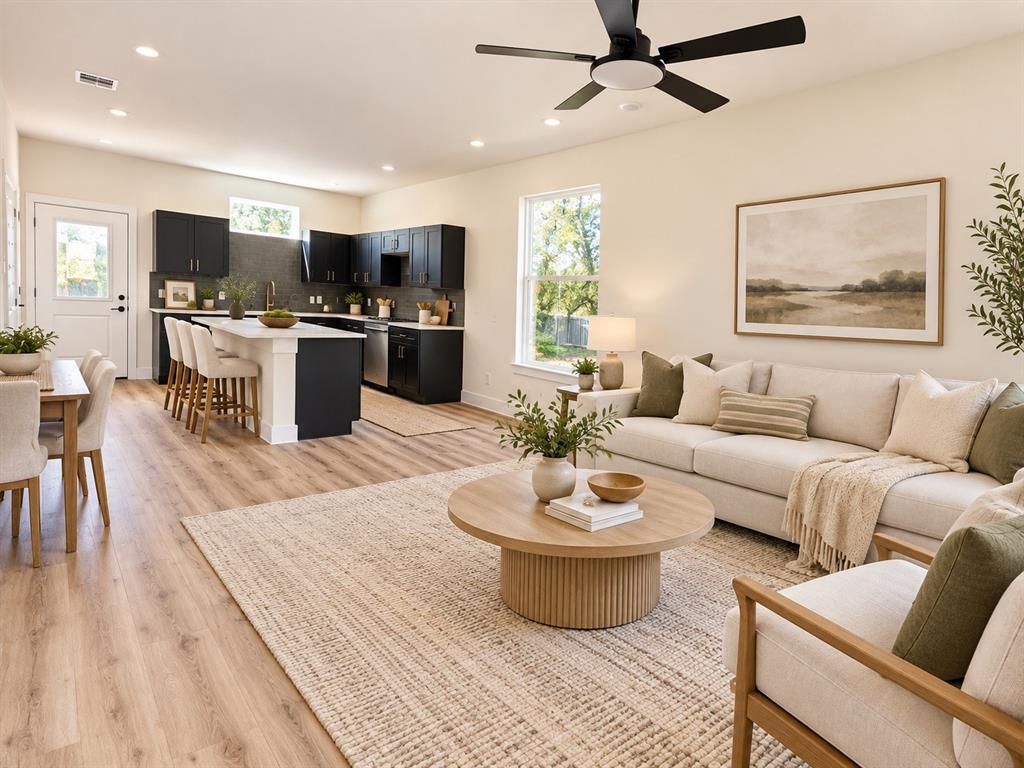 Open-concept living space featuring wood-finish flooring, recessed lighting, matte black ceiling fan, dark cabinetry with a central kitchen island, and white solid-surface countertops