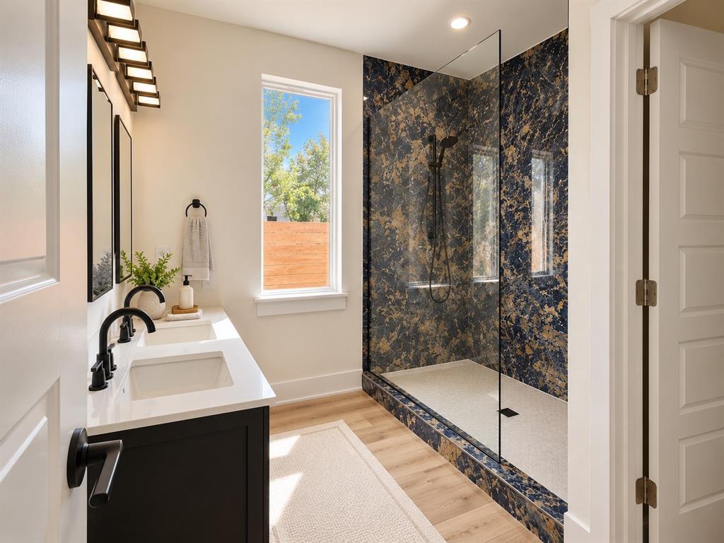 Dual-sink vanity with white countertops, dark cabinetry, matte black hardware, stone-finish shower surround, and walk-in glass-enclosed shower