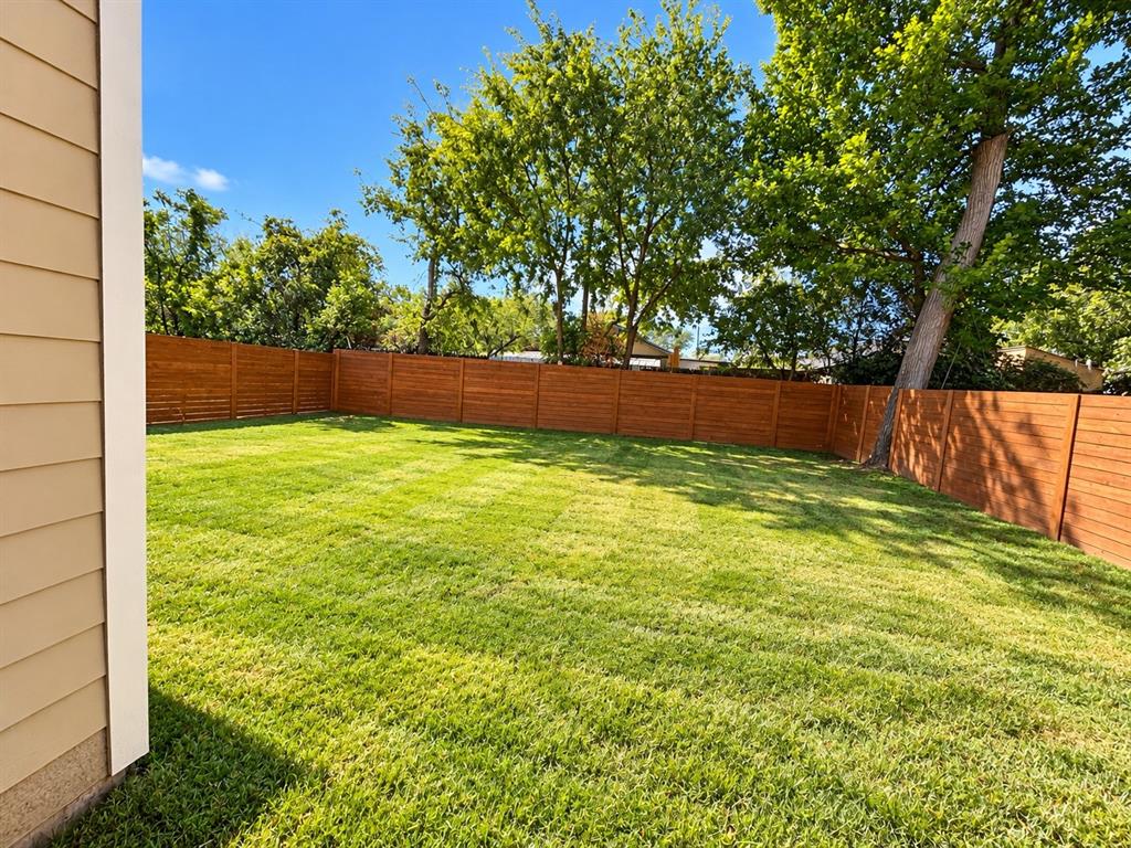 Spacious backyard featuring a manicured lawn, horizontal wood privacy fencing, and mature trees