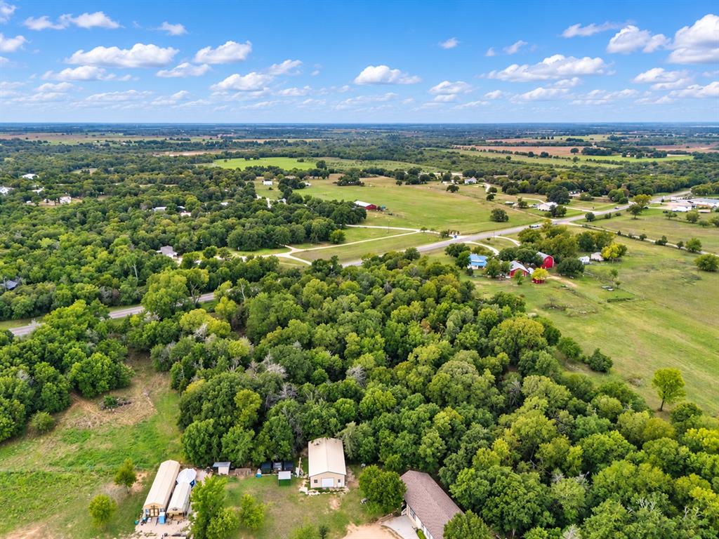 Aerial perspective of expansive acreage featuring mature tree clusters, open pasture land, and detached metal outbuildings