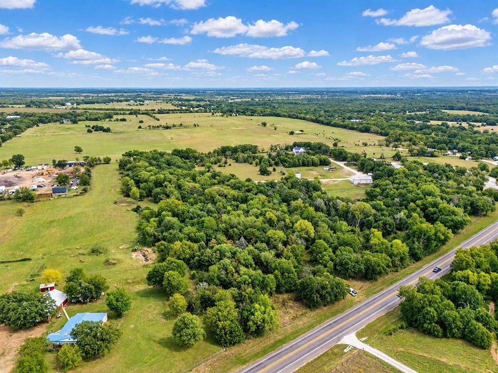 Aerial perspective of expansive acreage featuring mature tree stands, open pasture land, and direct frontage to a paved roadway