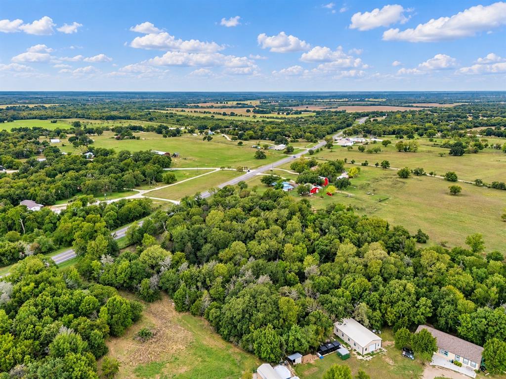 Aerial view of expansive acreage featuring mature hardwood trees, open pastureland, and multiple outbuildings