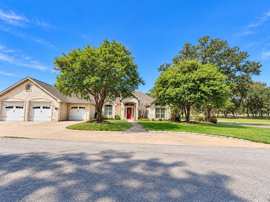Stone veneer exterior featuring an arched entryway, three-car garage, manicured lawn, and mature landscaping