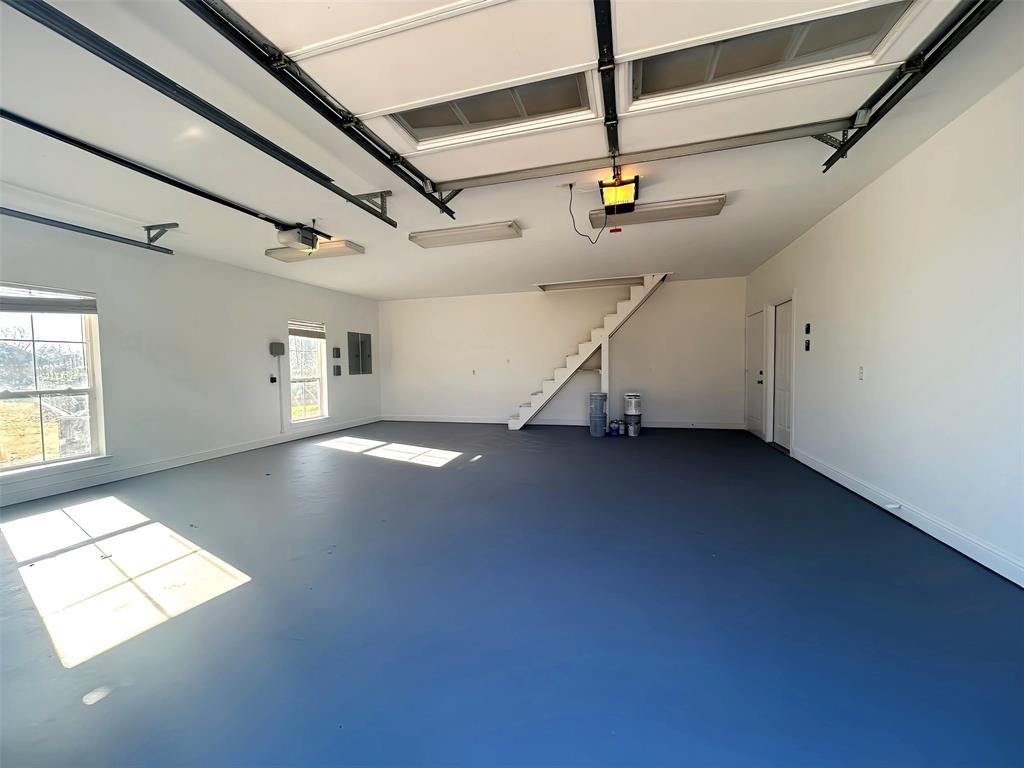 Spacious multi-car garage featuring finished epoxy flooring, dual windows, overhead lighting, and an integrated staircase