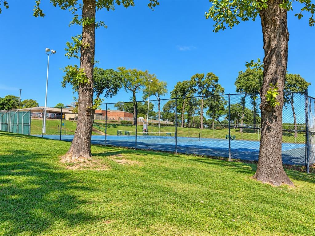 Tennis court featuring chain-link fencing, overhead illumination, and expansive green space