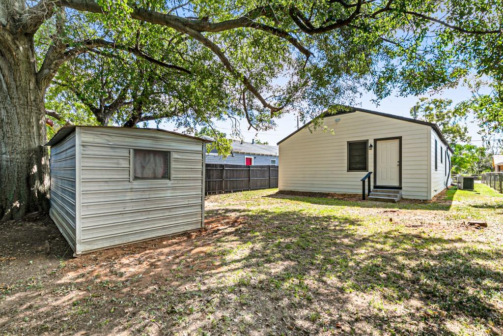 Rear exterior view featuring a spacious backyard, mature shade trees, and a separate storage shed.