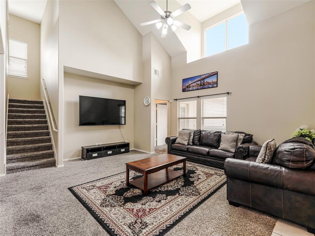 Vaulted ceilings, expansive windows, carpeted staircase with metallic handrail, and integrated ceiling fan with lighting fixture