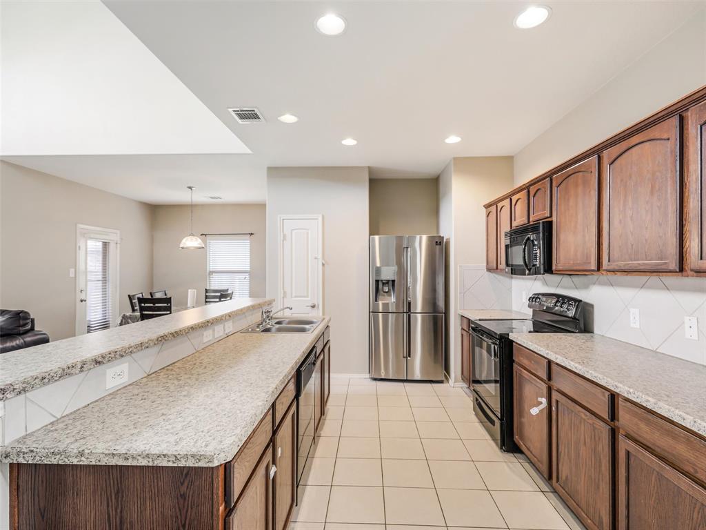 Kitchen featuring wood cabinetry, stone-finish countertops, stainless steel appliances, a double-basin sink, and tile flooring