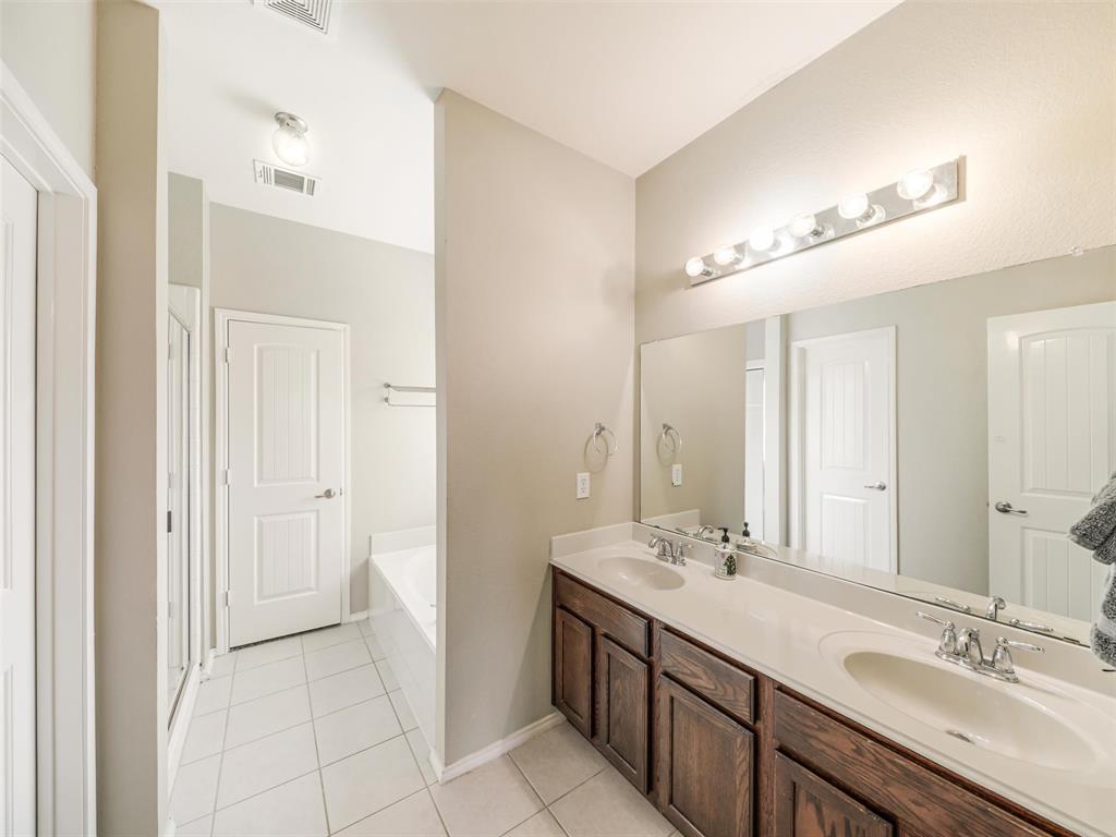 Dual-sink vanity with dark wood cabinetry, solid-surface countertop, full-width mirror, and integrated lighting
